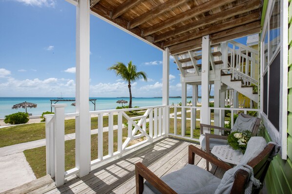 Une terrasse en bois offrant une vue sur l’océan, un espace salon couvert et un escalier menant à un niveau supérieur.