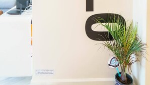 Una sala moderna con un cartel grande que dice 'HELLO', un sofá, una mesa de centro, un televisor y una planta en maceta.