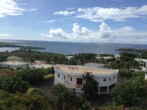 A coastal resort with multiple white buildings, a central white structure with a balcony, and a view of the sea and islands.