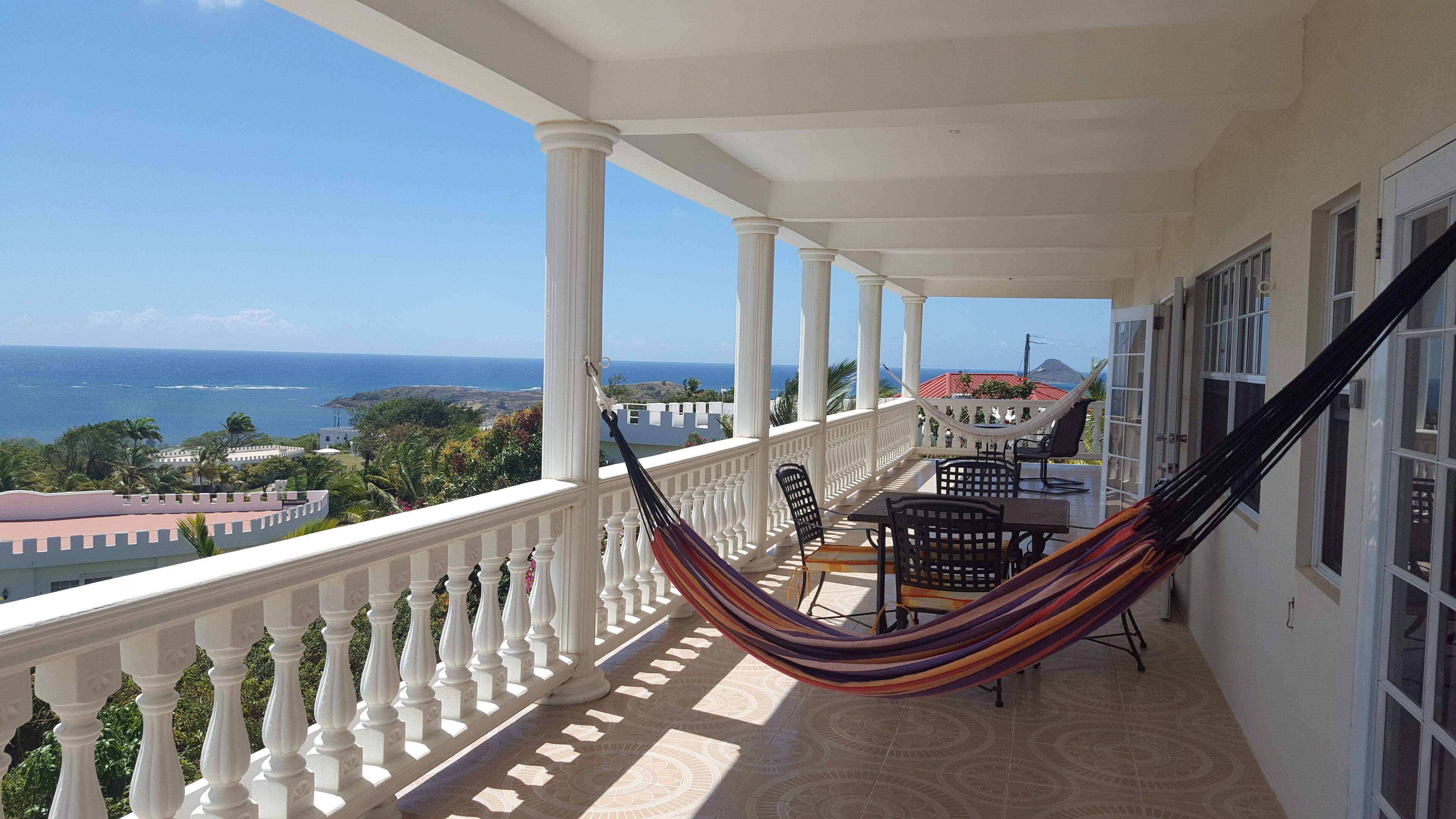 Uma varanda com vista para o oceano, uma rede e uma mesa com cadeiras.