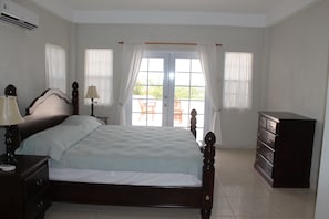 Quarto com cama, cômoda e vista para o exterior através de uma porta.