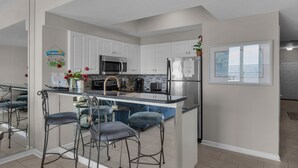 Una cocina moderna con armarios blancos, electrodomésticos de acero inoxidable y una isla central con taburetes.