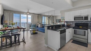 Una cocina moderna con una isla central, un área de comedor con vistas y una sala de estar con sofá y televisor.