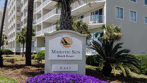Señal de Majestic Sun Beach Resort, con una palmera y flores púrpuras al frente.