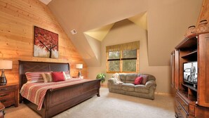 Een slaapkamer met een houten plafond, een groot bed, een bank en een televisie.