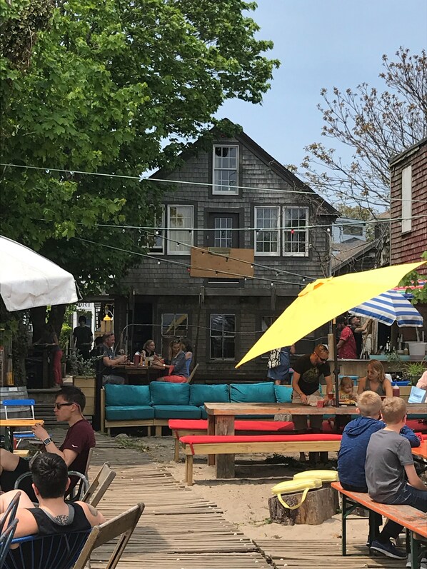 Un espacio al aire libre con bancos y mesas de madera, un sofá azul y un paraguas amarillo.