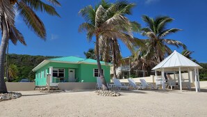 A beach house with a green roof, a white gazebo, and lounge chairs. - PLEASE COME AND RELAX ON OUR PRIVATE BEACH! (Cayman Brac)