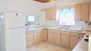 A kitchen with wooden cabinets, a white refrigerator, a stove, and a ceiling fan. - PLEASE COME AND RELAX ON OUR PRIVATE BEACH! (Cayman Brac)