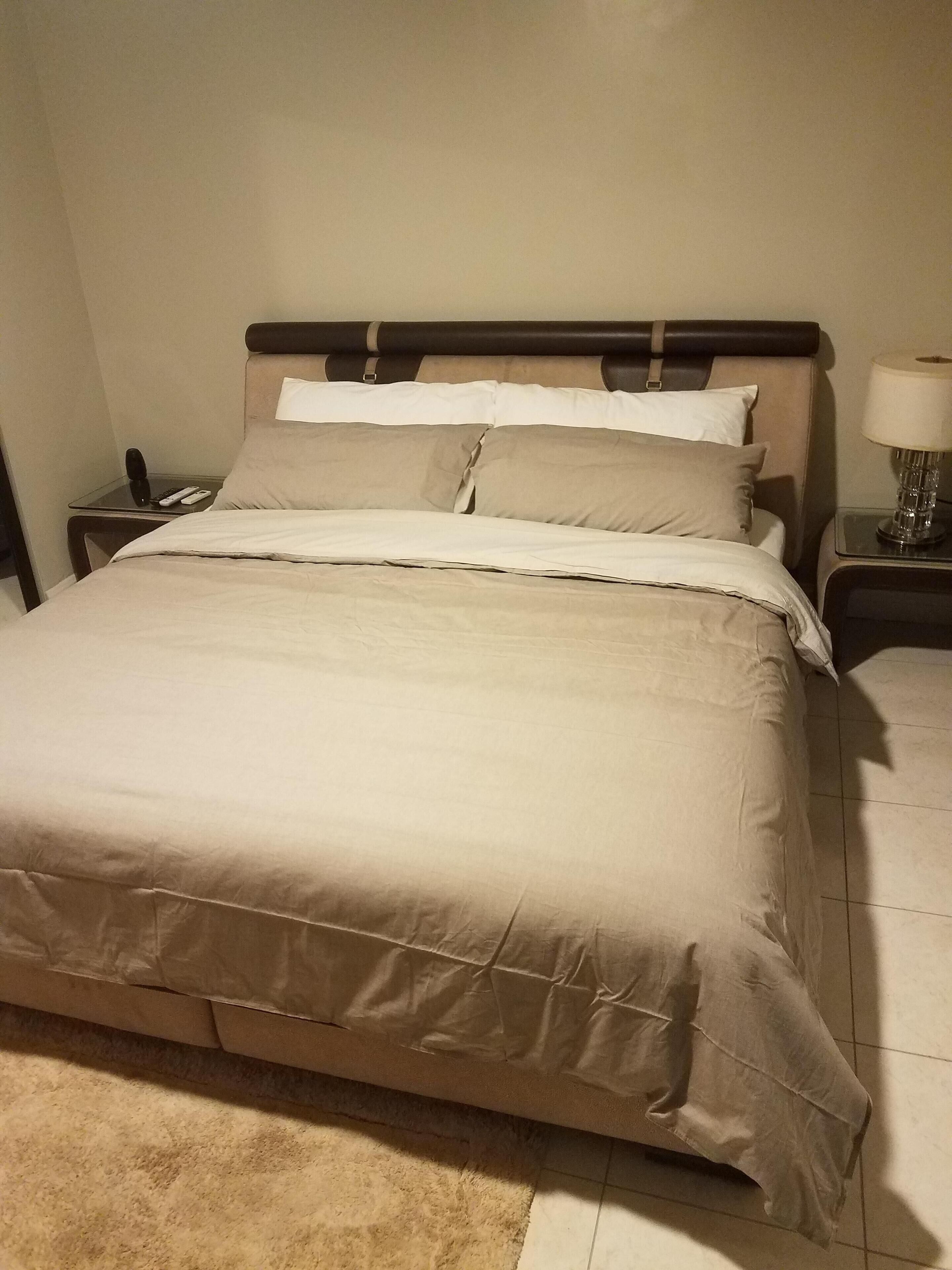 A neatly made bed with a beige comforter and pillows, a bedside table with a lamp, and a telephone.
