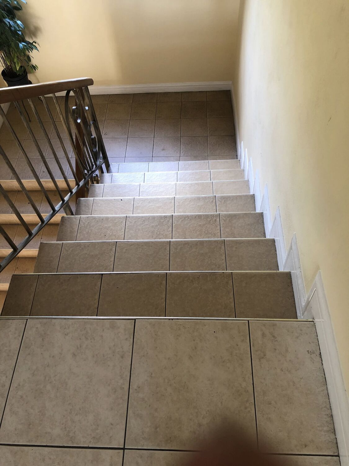 Un escalier recouvert de carreaux beiges et doté d’une rampe en métal, qui monte.