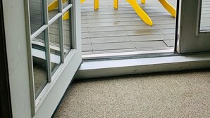 En vy genom en glasdörr ut mot en veranda med en gul Adirondack-stol och ett litet bord.