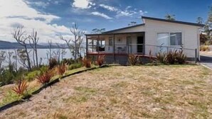A single-story house with a covered porch, a small deck, and a view of a lake. - Esperance Landing, waterfront luxury (Brooks Bay)
