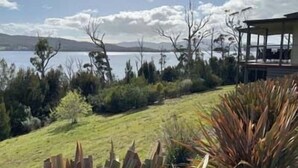 A lakeside property with a covered outdoor seating area, surrounded by vegetation and a view of the lake and distant mountains. - Esperance Landing, waterfront luxury (Brooks Bay)