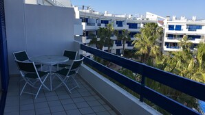 En balkon med et bord og stole, der giver udsigt over et boligområde med palmer og bygninger.