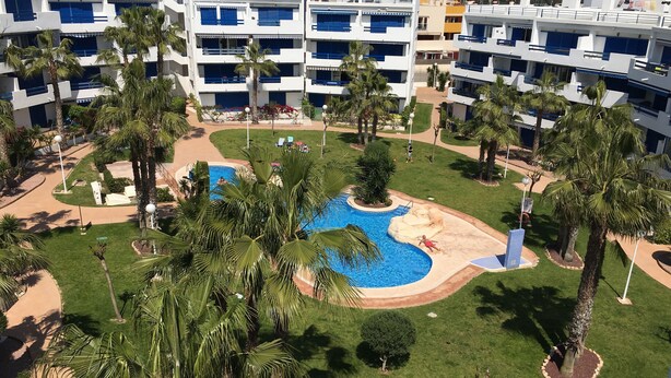 Et resort med flere hvide bygninger, en central pool og palmer.