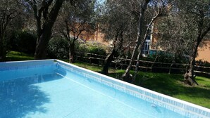 A swimming pool with a wooden deck, surrounded by trees and a fence. - three-room apartment with private garden (chiavari)