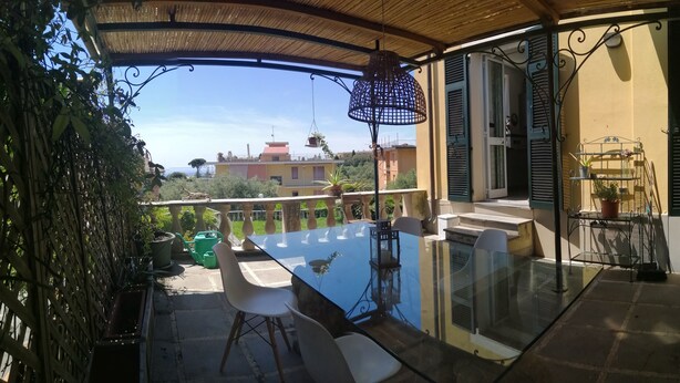 A glass-top table with chairs on a balcony with a view of buildings. - three-room apartment with private garden (chiavari)