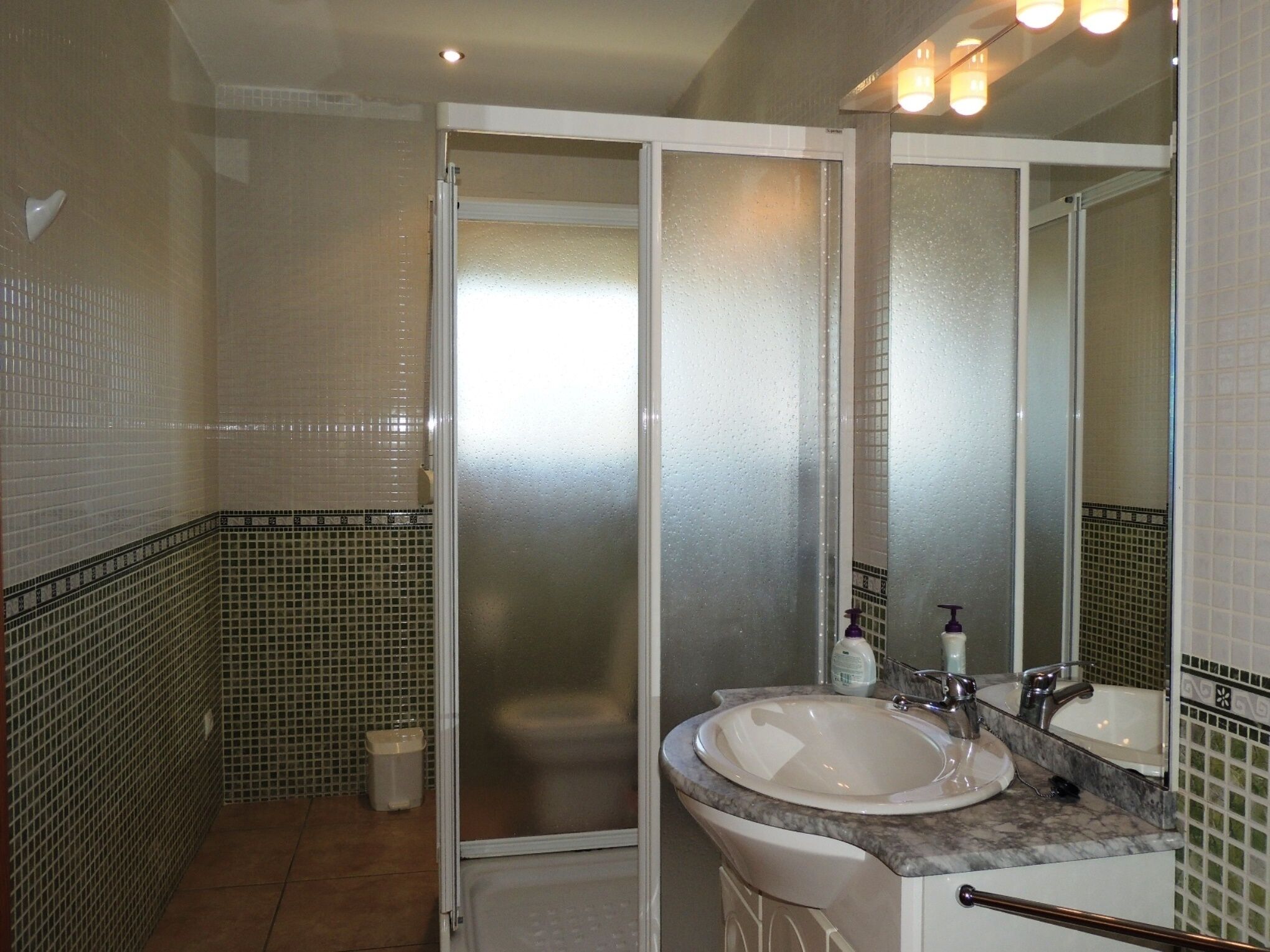 A bathroom with a glass shower door, a sink with a marble countertop, and a mirror above the sink.