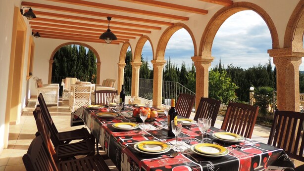 Un espace extérieur aménagé pour les repas, doté d’une pergola couverte, d’arcs en pierre et offrant une vue sur la verdure environnante.