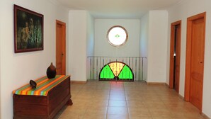 Un couloir avec un banc en bois, un tableau accroché au mur et une porte ornée d’un vitrail.