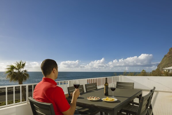 A man in a red shirt sitting at a table with a view of the ocean, plates of food, and wine glasses. - Holiday house by the sea. (Calheta/ Madeira)