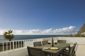 A dining table with chairs and plates of food, a bottle of wine, and a glass of wine on a balcony overlooking the ocean. - Holiday house by the sea. (Calheta/ Madeira)