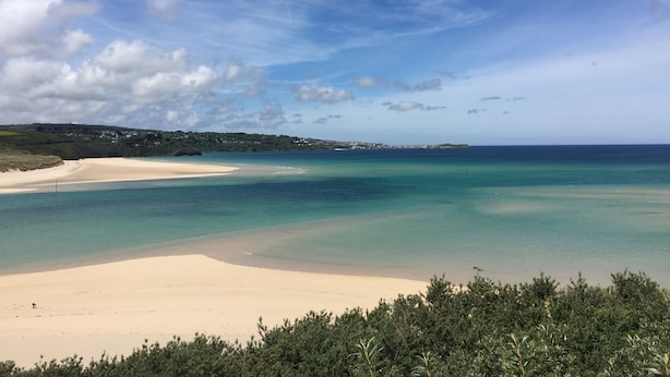 Una playa con aguas turquesas cristalinas, una orilla arenosa y una vista distante de un pueblo.
