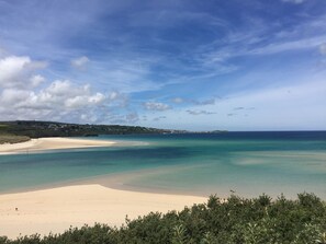 A beach with clear turquoise waters, a sandy shore, and a distant view of a town. - Converted Barn, Rural Location, Near Coast, Parking & Dog Friendly (Goldsithney)
