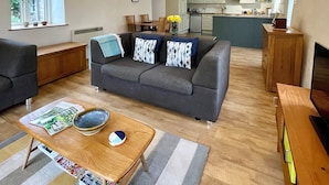 Una sala moderna con un sofá gris, una mesa de centro de madera y una cocina al fondo.
