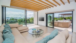 A modern living room with a large sofa, a glass coffee table, and a view of a patio with outdoor furniture.