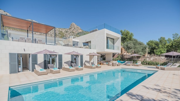 A modern pool area with lounge chairs and umbrellas, surrounded by a pool and a building with large windows.