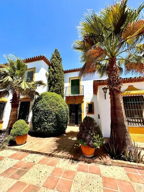 A white building with a tiled patio, palm trees, and a well-maintained garden.