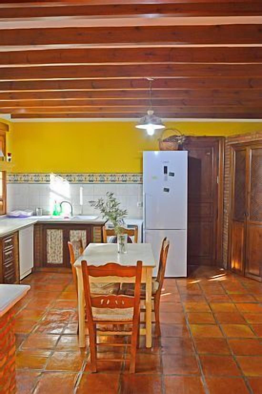 A kitchen with a tiled floor, wooden cabinets, a white refrigerator, and a dining table with chairs.