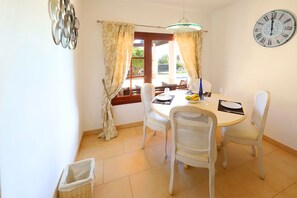 A dining area with a round table, white chairs, a clock on the wall, and a window with curtains. - Luxury 4-bedroom, 4 bathroom villa in exclusive Los Mojones area, with Jacuzzi (Tías)