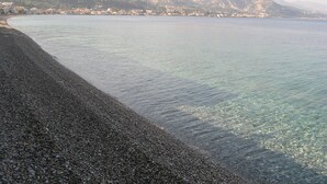 A pebble beach with clear water and a town in the background. - Luxury Private Villa With Large Pool And Amazing Views  (Corinth)