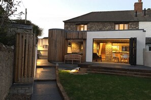 A modern house with a stone facade, a wooden deck, and a well-lit interior. - Luxury Cottage, less than 5 mins walk to the North Cornwall Coast (Bude, Cornwall)