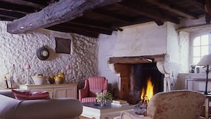 A rustic living room with exposed wooden beams, a stone wall, a fireplace, and traditional furniture. - Exquisite Farmhouse & Heated Pool (Lusignac)
