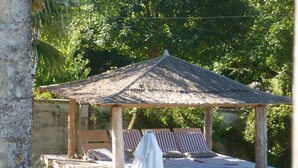 A wooden gazebo with a thatched roof, a bed with striped bedding, and a white canopy. - Exquisite Farmhouse & Heated Pool (Lusignac)