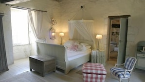 A bedroom with a bed, a bedside table, a chair, a small table, and a window with curtains. - Exquisite Farmhouse & Heated Pool (Lusignac)