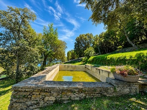 Estany amb revestiment de pedra i mur de pedra en un parc frondós i verd.