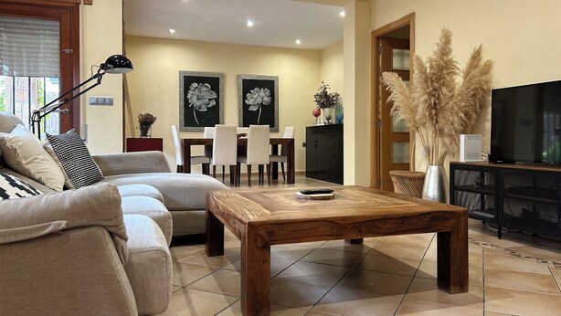 A living room with a sofa, a wooden coffee table, a TV, and a dining area with chairs and a table.