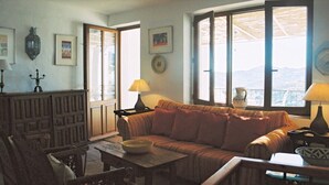 A cozy living room with a sofa, a wooden table, and a view of the mountains through large windows. - Large Four bedroom house in exquisite 16th century Moorish village. Sleeps 8. (Frigiliana, Nerja)