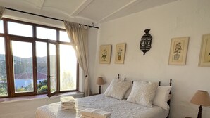 A spacious bedroom with a large bed, a wooden nightstand, and a view of the outdoors through a large window. - Large Four bedroom house in exquisite 16th century Moorish village. Sleeps 8. (Frigiliana, Nerja)