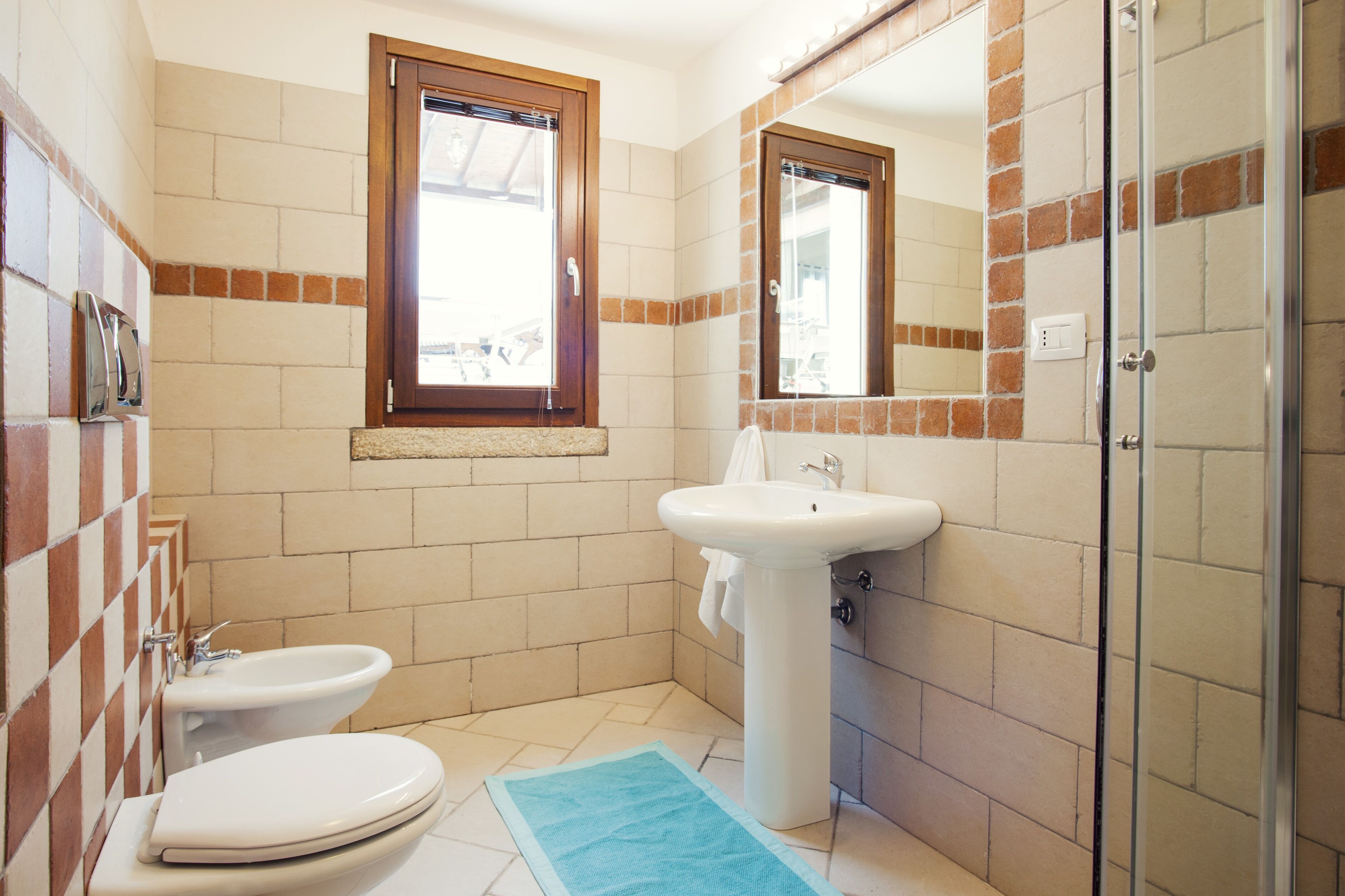 Een badkamer met toilet, bidet, wastafel en een douchecabine van glas.
