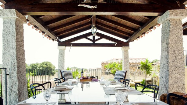 A covered outdoor dining area with a table set for four, surrounded by stone pillars, under a wooden roof structure. - Beautiful Villa Layla with pool (Castiadas)