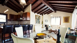 A spacious living area with a high ceiling, wooden beams, a dining table with chairs, and a kitchen in the background. - Beautiful Villa Layla with pool (Castiadas)