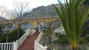 A staircase leading to a building with a yellow facade, surrounded by trees and a mountain in the background. - Villa 15min from Alicante, free WiFi, indoor pool, ideal for families.  (Tibi)