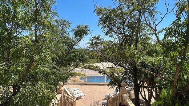 A view of a pool area with a covered deck, surrounded by lush greenery and a decorative archway. - Villa 15min from Alicante, free WiFi, indoor pool, ideal for families.  (Tibi)