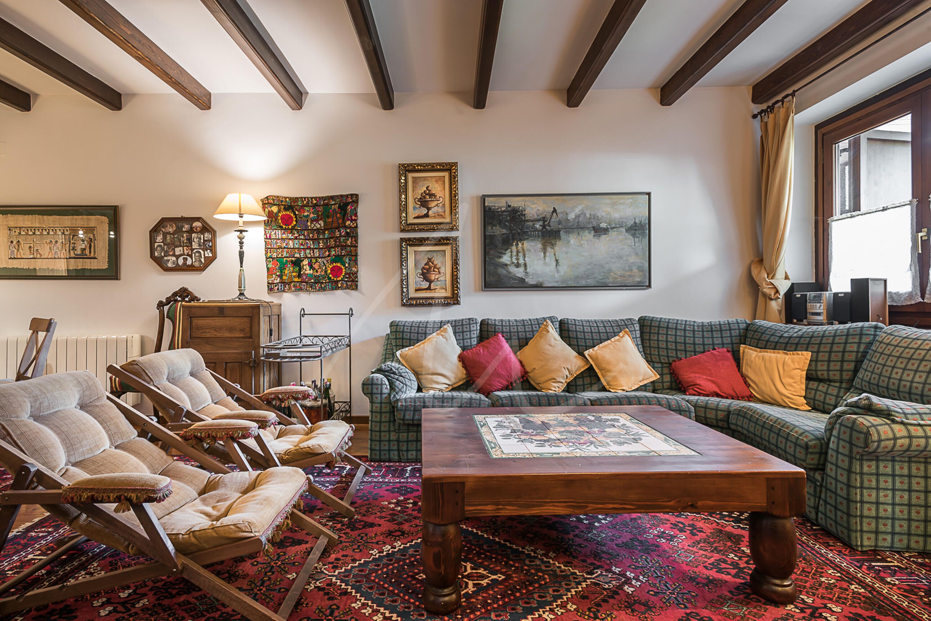 Una sala de estar acogedora con un sofá verde estampado, sillones de madera, una mesa de centro de madera y un tapete rojo estampado.
