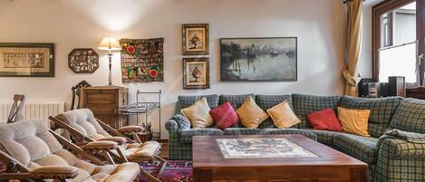 Una sala de estar acogedora con un sofá verde estampado, sillones de madera, una mesa de centro de madera y un tapete rojo estampado.
